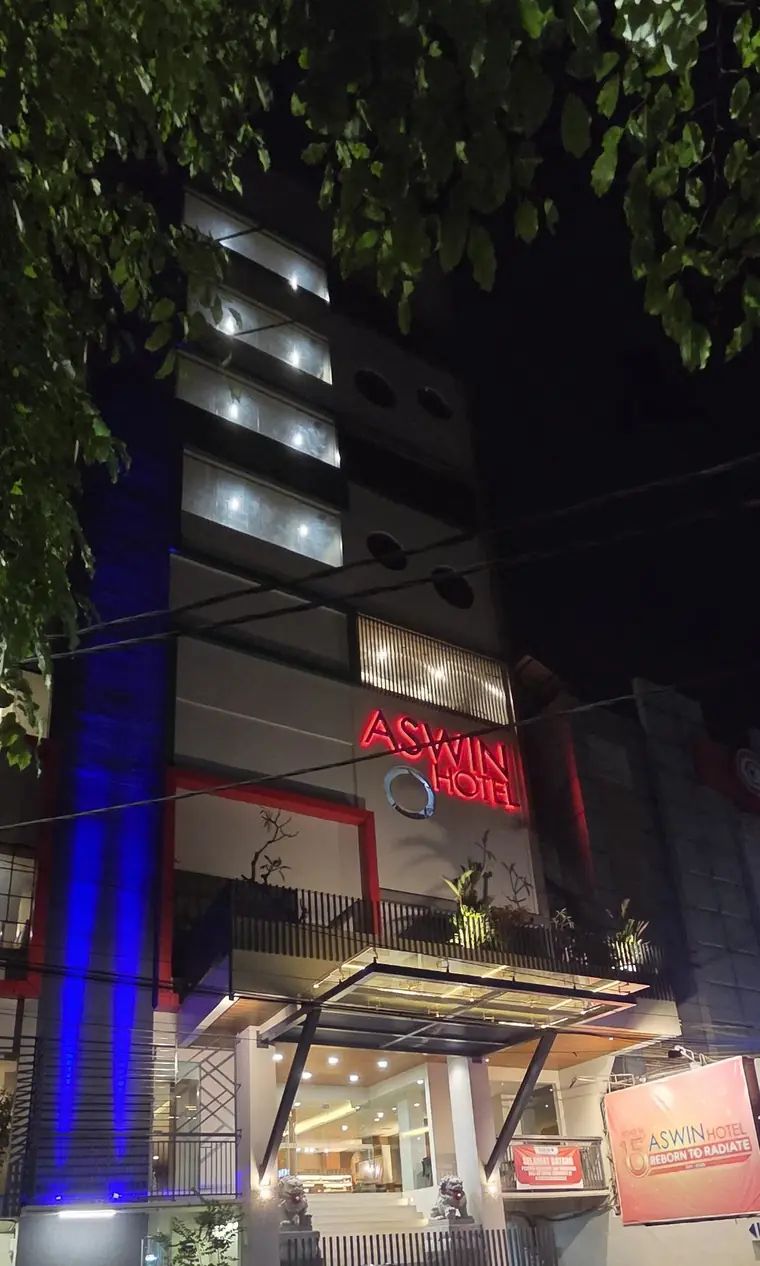 Fasad Aswin Hotel dengan papan nama menyala di malam hari